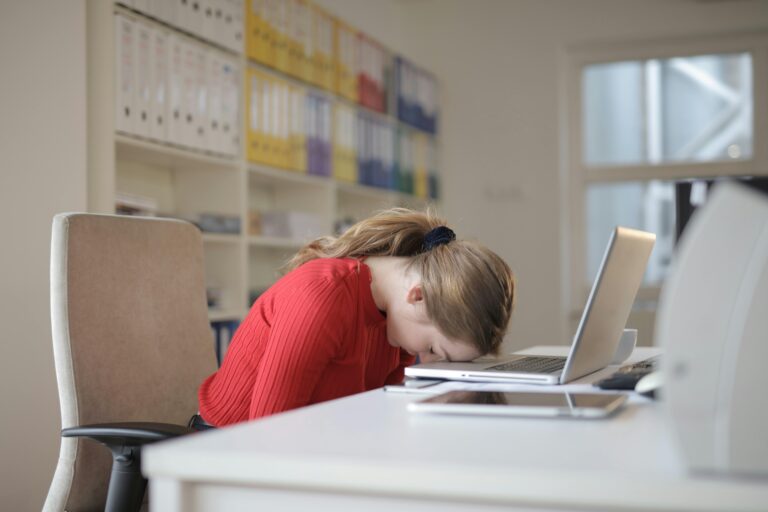 Tired woman resting her forehead on a computer at her desk, showing burnout and exhaustion